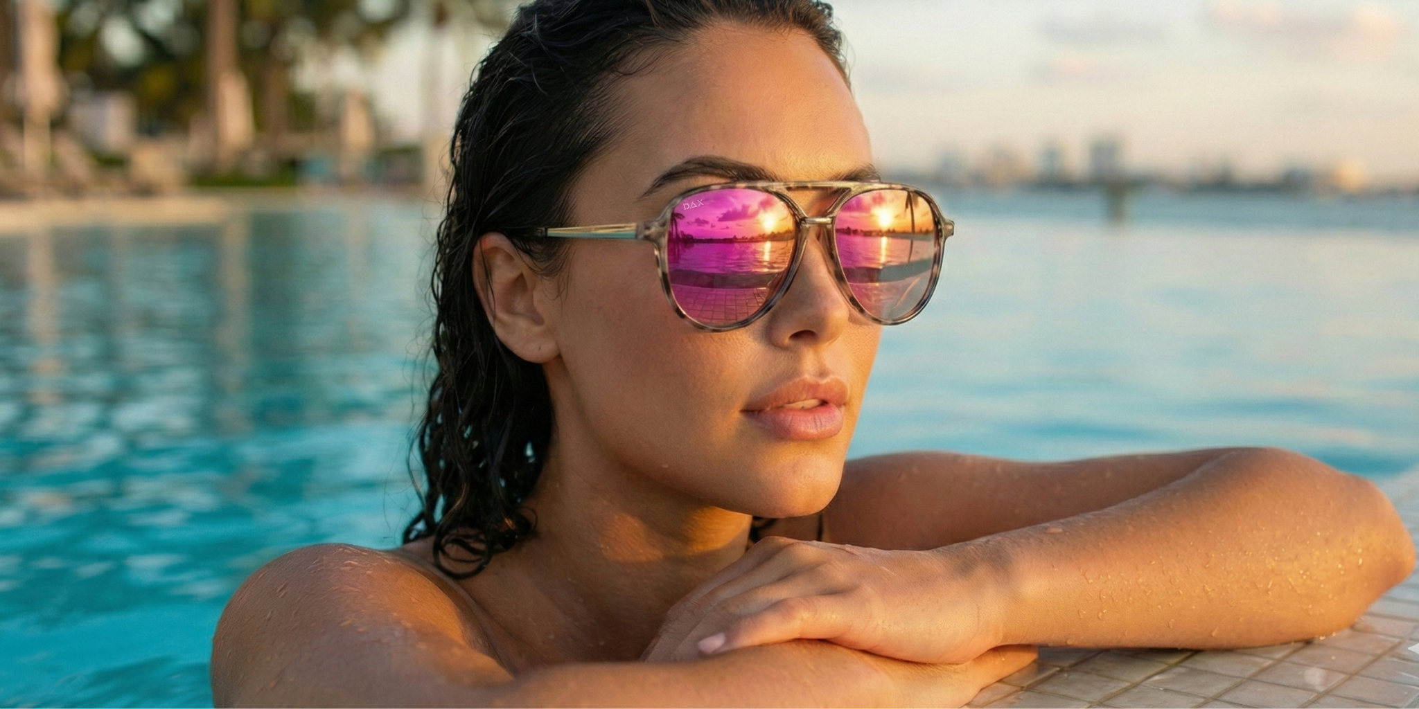 An wide image of a woman in a pool wearing large, pink mirrored, sunglasses.