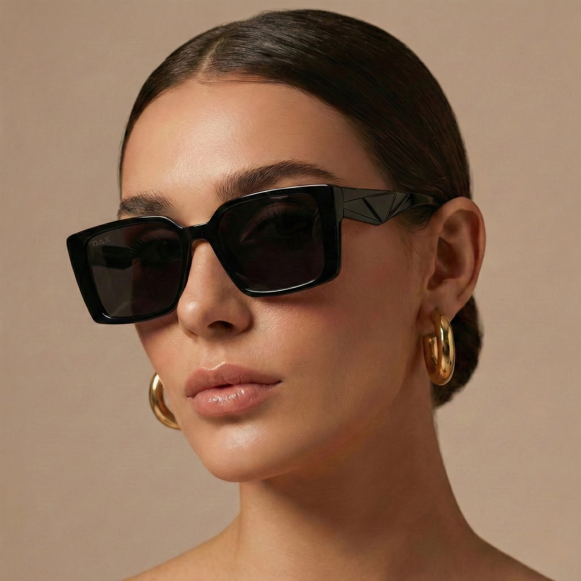 Woman wearing black sunglasses and gold hoop earrings against a beige background