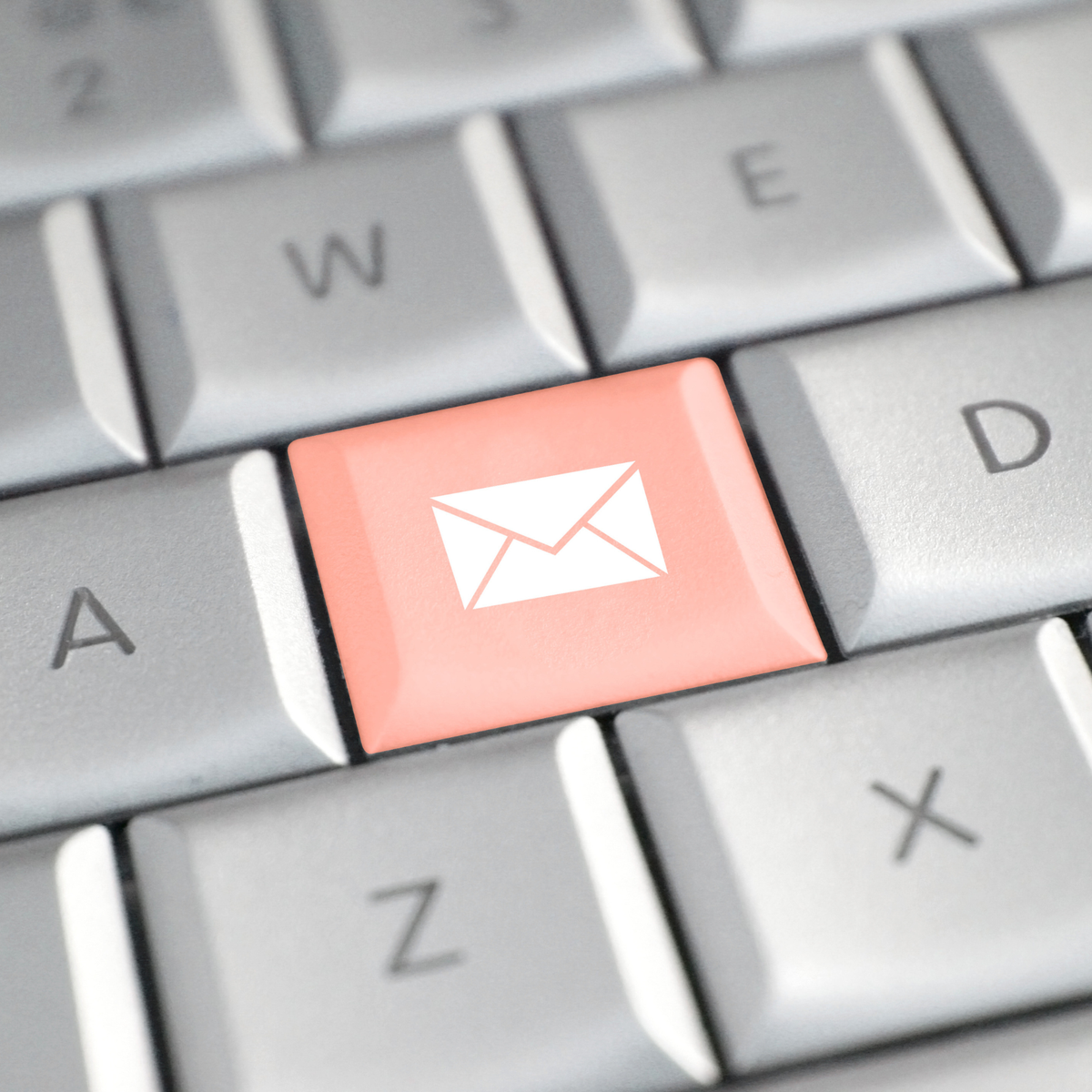 A close-up of a computer keyboard with a coral pink key in the center featuring a white envelope icon, surrounded by gray lettered keys.