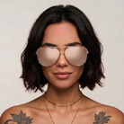 Woman wearing large gold aviator sunglasses with a neutral background