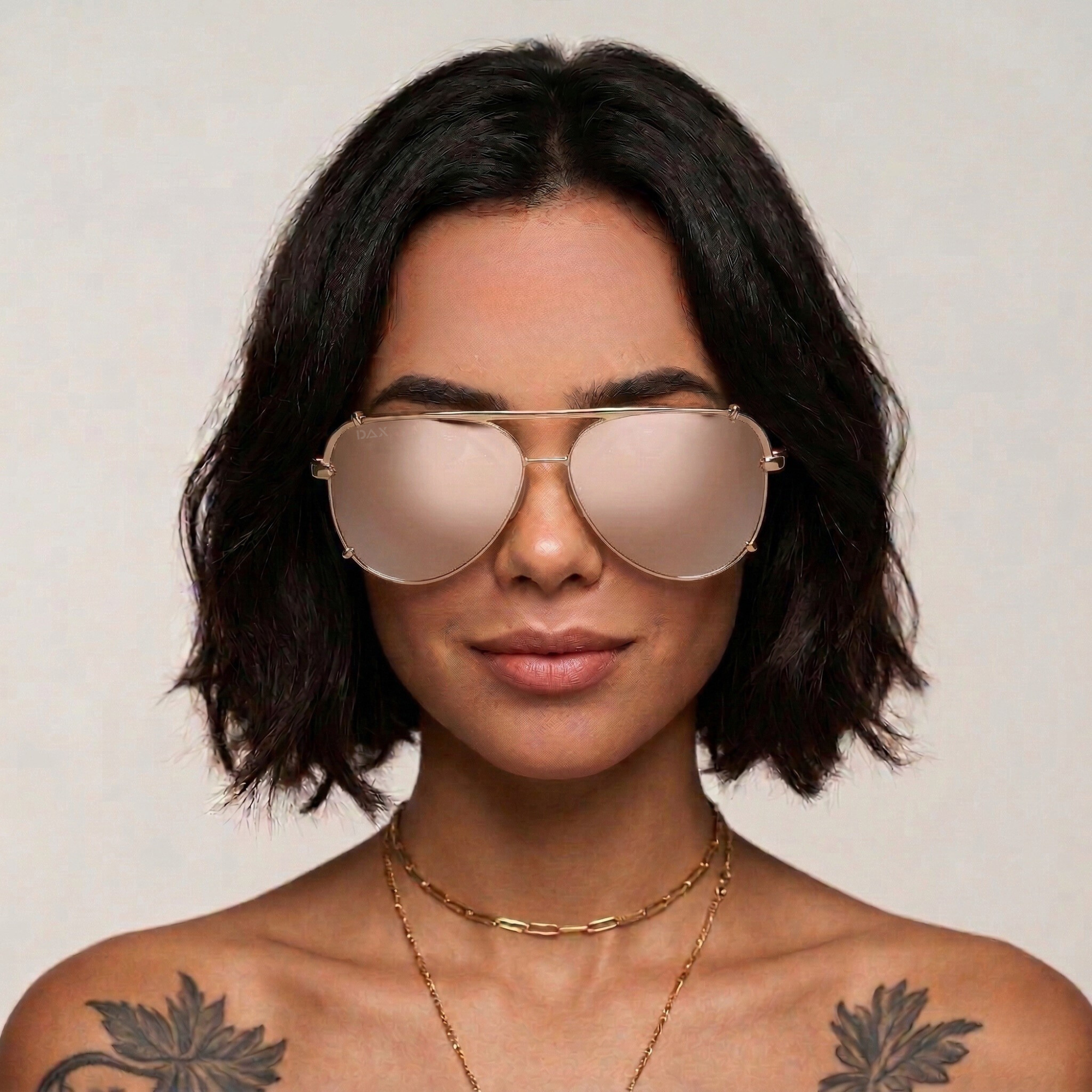 Woman wearing large gold aviator sunglasses with a neutral background