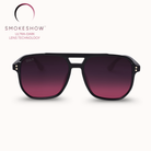 A pair of aviator-style sunglasses with a matte black frame and gradient dark purple to magenta lenses, shown against a light cream background with the Smokeshow brand logo in the upper left.